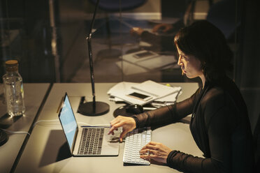 High angle view of businesswoman using laptop at desk in office during night - MASF02424