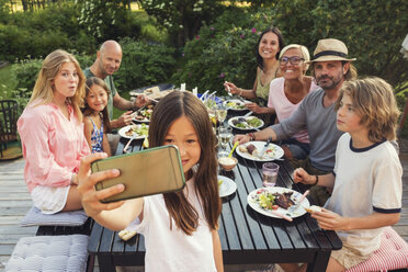 Glückliche Familie und Freunde schauen, während das Mädchen ein Selfie vom Handy im Hinterhof während einer Gartenparty macht - MASF02427