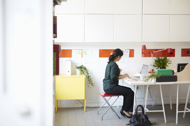 Volle Länge Seitenansicht der Geschäftsfrau mit Dokument und Laptop am Tisch im Büro - MASF02435
