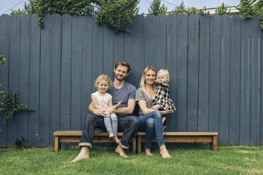 Full length portrait of happy parents and children sitting on seats against fence at yard - MASF02451
