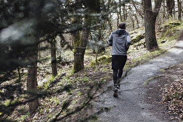 Full length rear view of male athlete jogging on narrow road in forest - MASF02458