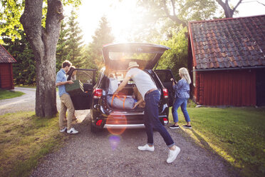 Full length of friends loading luggage into car on road during sunny day - MASF02464