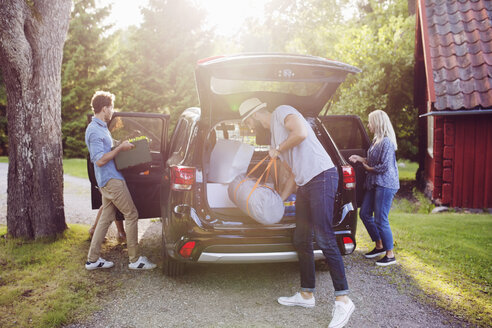 Freunde laden an einem sonnigen Tag in voller Länge Gepäck ins Auto - MASF02465