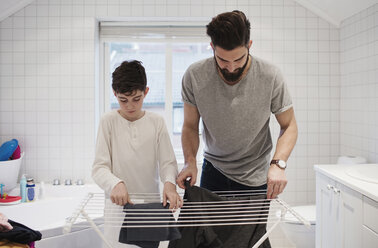 Father and son drying clothes on rack at home - MASF02466