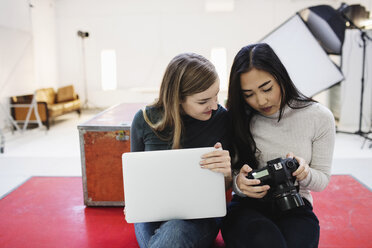 Female bloggers watching photographs on digital camera in office - MASF02480