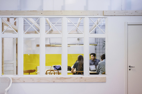 Vier Personen diskutieren in einer Besprechung, gesehen durch ein Glasfenster im Büro, lizenzfreies Stockfoto