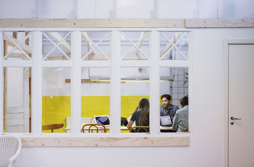 Vier Personen diskutieren in einer Besprechung, gesehen durch ein Glasfenster im Büro - MASF02486