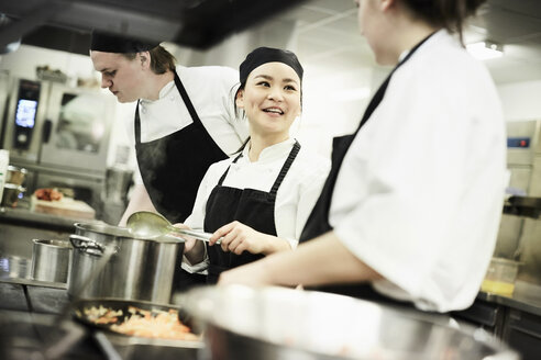 Weibliche Köchin beim Kochen von Speisen im Gespräch mit einem Kollegen in einer Großküche - MASF02492