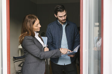 Eine Immobilienmaklerin hilft einem Mann, während sie auf eine Broschüre am Fenster zeigt - MASF02496