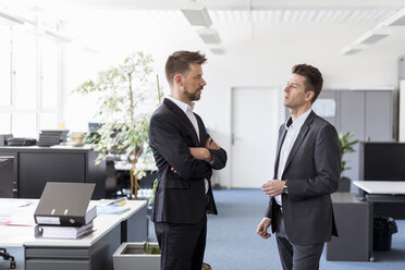 Zwei Geschäftsleute stehen in einem Büro und diskutieren über Lösungen - DIGF03885