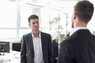 Zwei Geschäftsleute stehen in einem Büro und diskutieren über Lösungen - DIGF03887