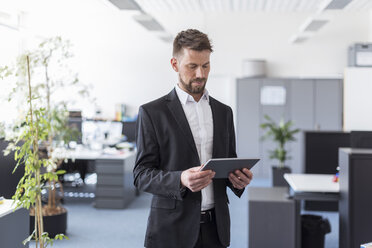 Erfolgreicher Geschäftsmann im Büro stehend, mit digitalem Tablet - DIGF03888