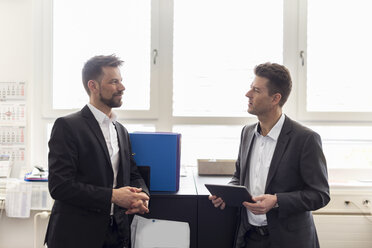 Two businessmen standing in office, discussing solutions, using digital tablet - DIGF03891