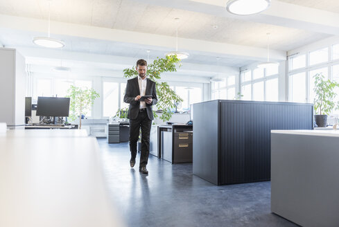 Businessman walking in office, using digital tablet - DIGF03897