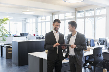 Two businessmen standing in office, discussing solutions, using digital tablet - DIGF03898