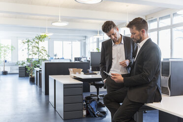 Zwei Geschäftsleute stehen in einem Büro, diskutieren Lösungen und benutzen ein digitales Tablet - DIGF03899