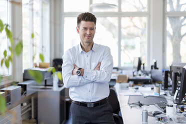 Portrait of a successful businessman standing in office with arms crossed - DIGF03904