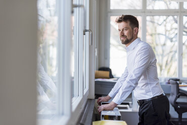 Porträt eines erfolgreichen Geschäftsmannes, der im Büro sitzt und aus dem Fenster schaut - DIGF03905