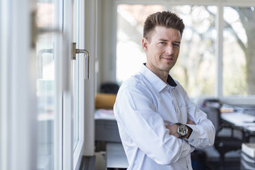 Portrait of a successful businessman standing in office with arms crossed - DIGF03906