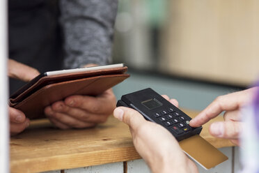 Ausgeschnittenes Bild eines Kunden, der mit einem Kartenlesegerät bezahlt, während der Besitzer ein digitales Tablet in einem Imbisswagen benutzt - MASF02518