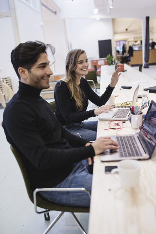 Cheerful young woman and man looking away while sitting at desk in office stock photo