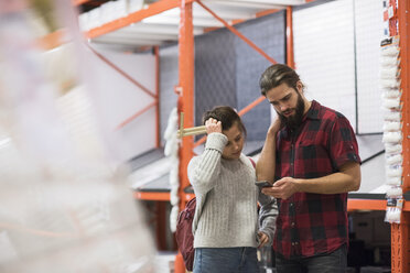 Couple using smart phone while standing in hardware store - MASF02524