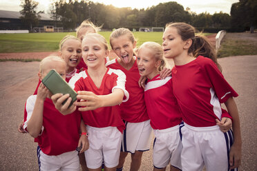 Cheerful soccer girls taking selfie on footpath against field - MASF02538