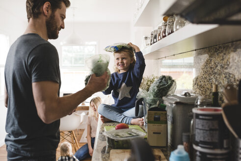 Father and daughter cooking food in kitchen with family in background at home - MASF02540