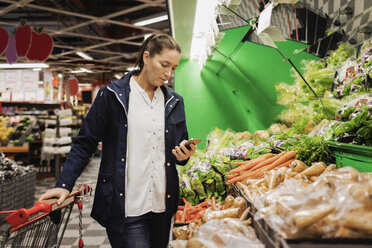 Frau benutzt Smartphone beim Einkaufen von Lebensmitteln im Supermarkt - MASF02552