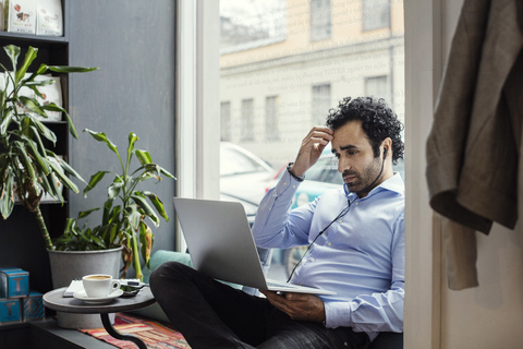Worried businessman using laptop while sitting by window in office stock photo