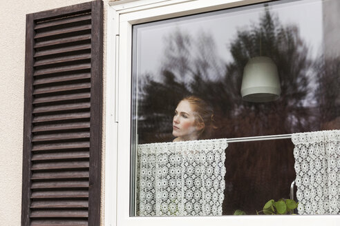 Frau schaut durch ein Fenster, während sie zu Hause steht - MASF02562