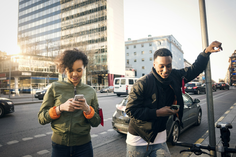 Teenagers using phone while standing on sidewalk by city street stock photo