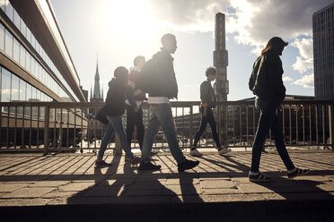 Teenagers walking on bridge by railing in city on sunny day - MASF02570