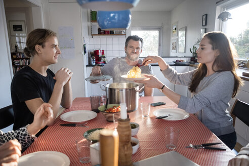 Woman serving food in plate while sitting with family at dining table - MASF02581