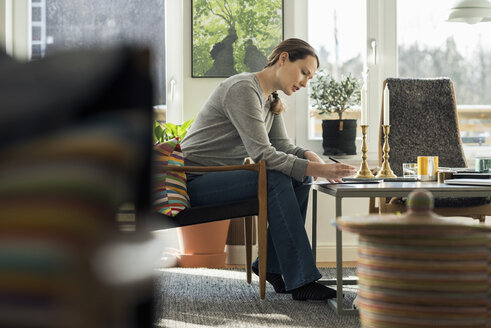 Woman sitting with document at home - MASF02583