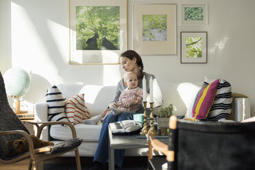 Woman sitting with baby girl on sofa at home - MASF02587