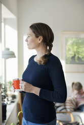 Woman standing with coffee cup in living room at home - MASF02588