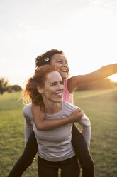 Woman giving piggyback to daughter at park against sky during sunset - MASF02604