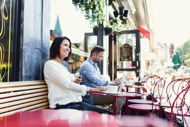 Thoughtful businesswoman holding smart phone while sitting at sidewalk cafe - MASF02615