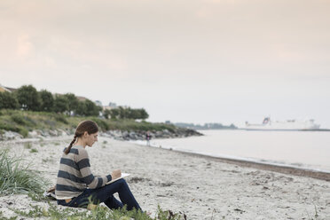 Woman writing on book while sitting at beach against sky - MASF02616