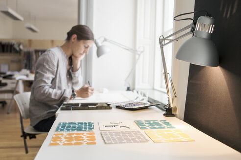 Frau malt auf Leinwand vor beleuchteter Schreibtischlampe im Kreativbüro - MASF02617