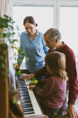 Frau sieht Junge und Urgroßvater beim Klavierspielen an, lizenzfreies Stockfoto