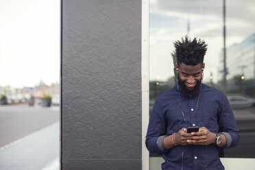 Junger Mann hört Musik von einem Mobiltelefon am Fenster - MASF02624