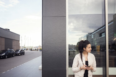 Junge Frau, die ihr Smartphone benutzt und dabei gegen das Fenster schaut - MASF02625