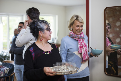 Frauen halten Serviertablett und Schüssel, Männer stehen im Hintergrund, lizenzfreies Stockfoto