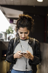 Woman listening music through smart phone in city - MASF02640