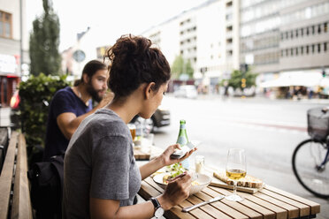 Frau isst in einem Straßencafé in der Stadt und benutzt dabei ein Mobiltelefon - MASF02641