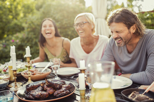 Fröhliches Paar und Freundin lachend am Esstisch während einer Gartenparty im Hinterhof - MASF02643