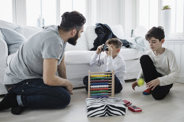 Junge fotografiert Vater, der mit seinem Bruder im Wohnzimmer mit einem Ball spielt - MASF02653