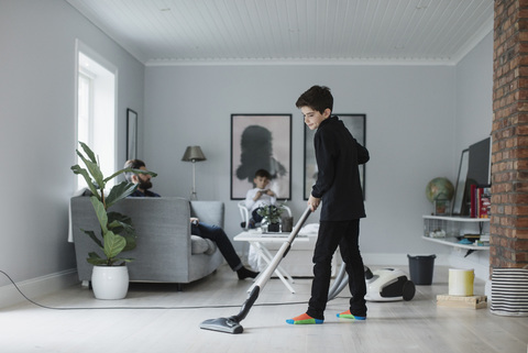 Junge staubsaugt Boden im Wohnzimmer zu Hause, lizenzfreies Stockfoto